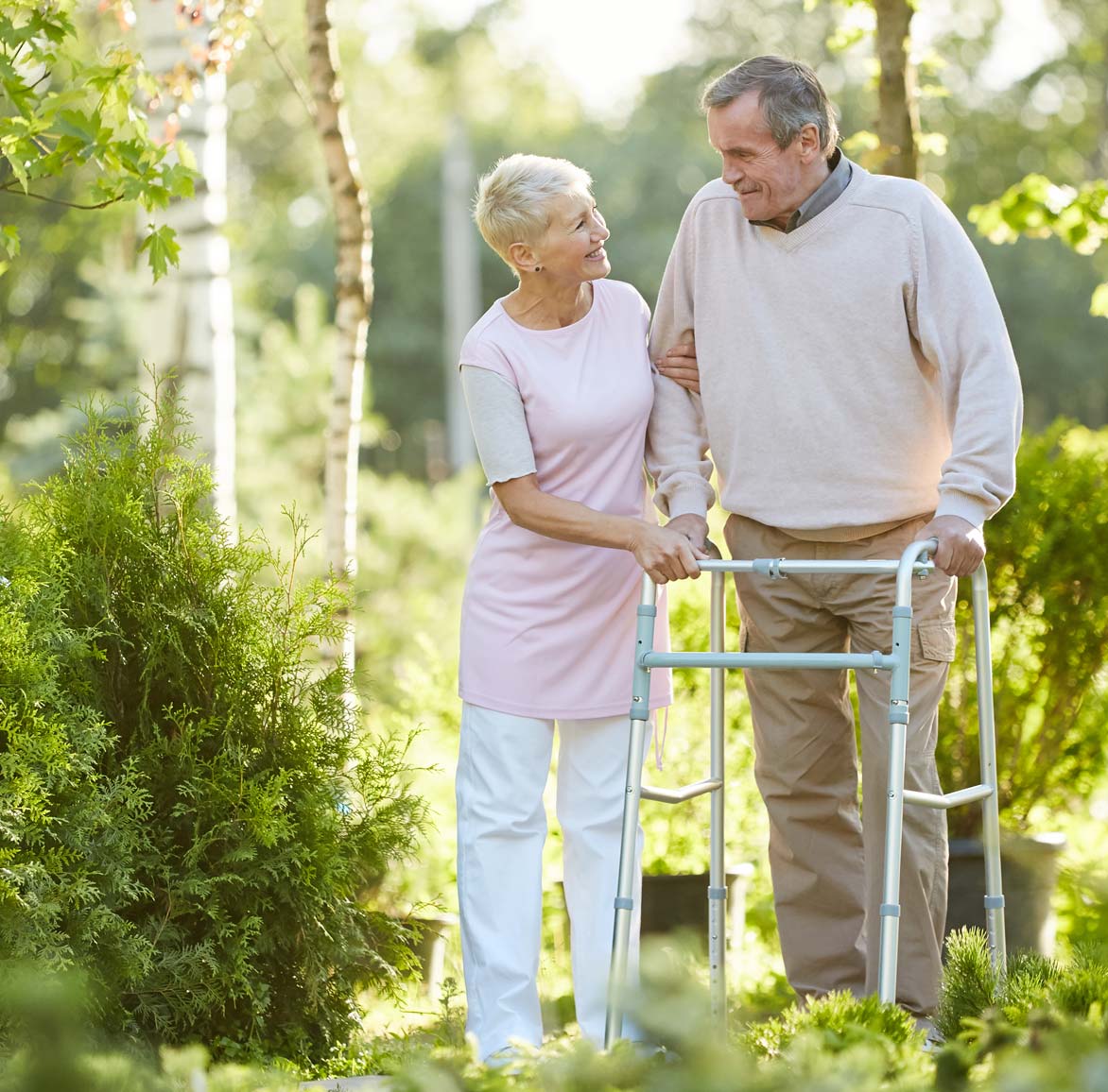 Couple walking in a park-like setting. The man is using a walker to assist his walk.